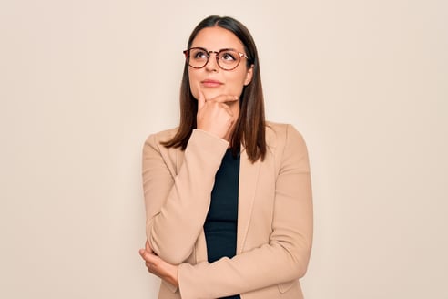 woman wearing glasses and beige blazer thinking